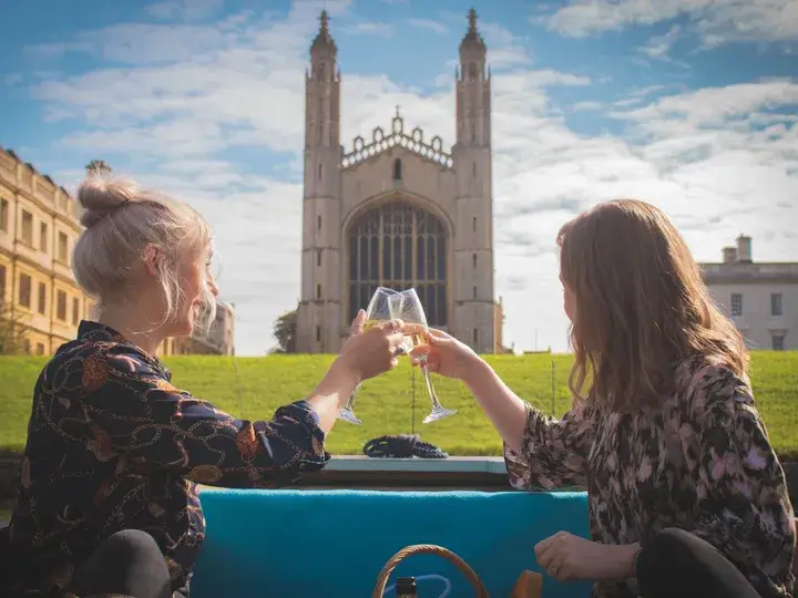 Two young women toasting champagne glasses with King's College Chapel, an impressive stone building, in the background.