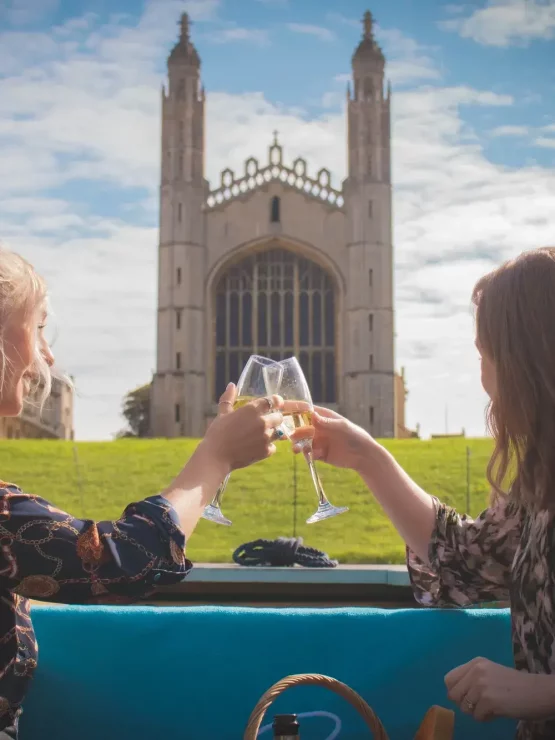 Two young women toasting champagne glasses with King's College Chapel, an impressive stone building, in the background.
