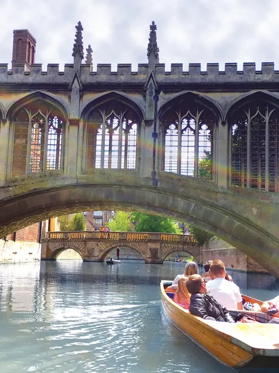 A party of people in a punting boat beneath the Bridge of Sighs, an ornately carved, arched stone bridge.