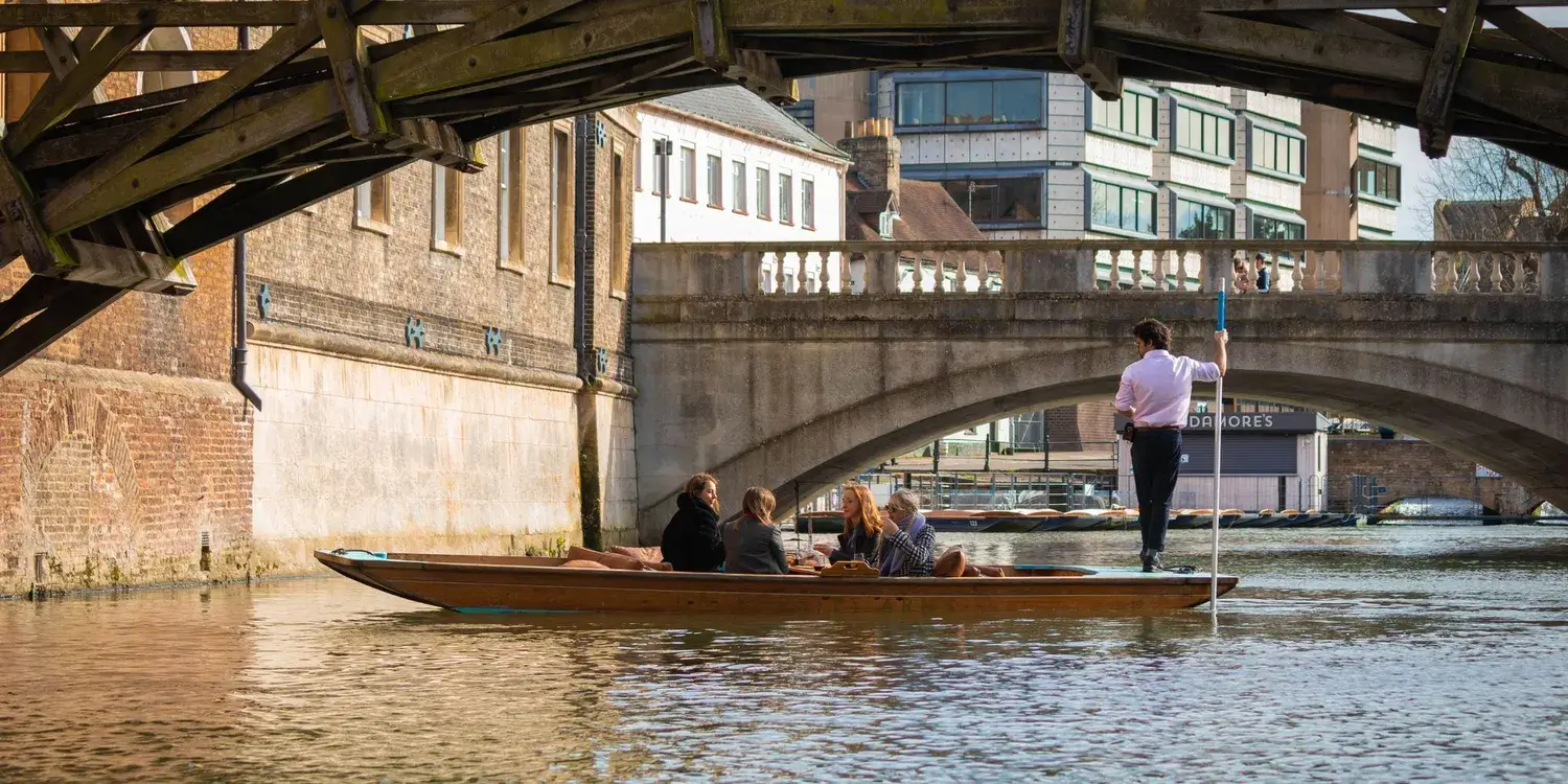 A photo of a party of people in a punting boat, framed by an arched bridge.
