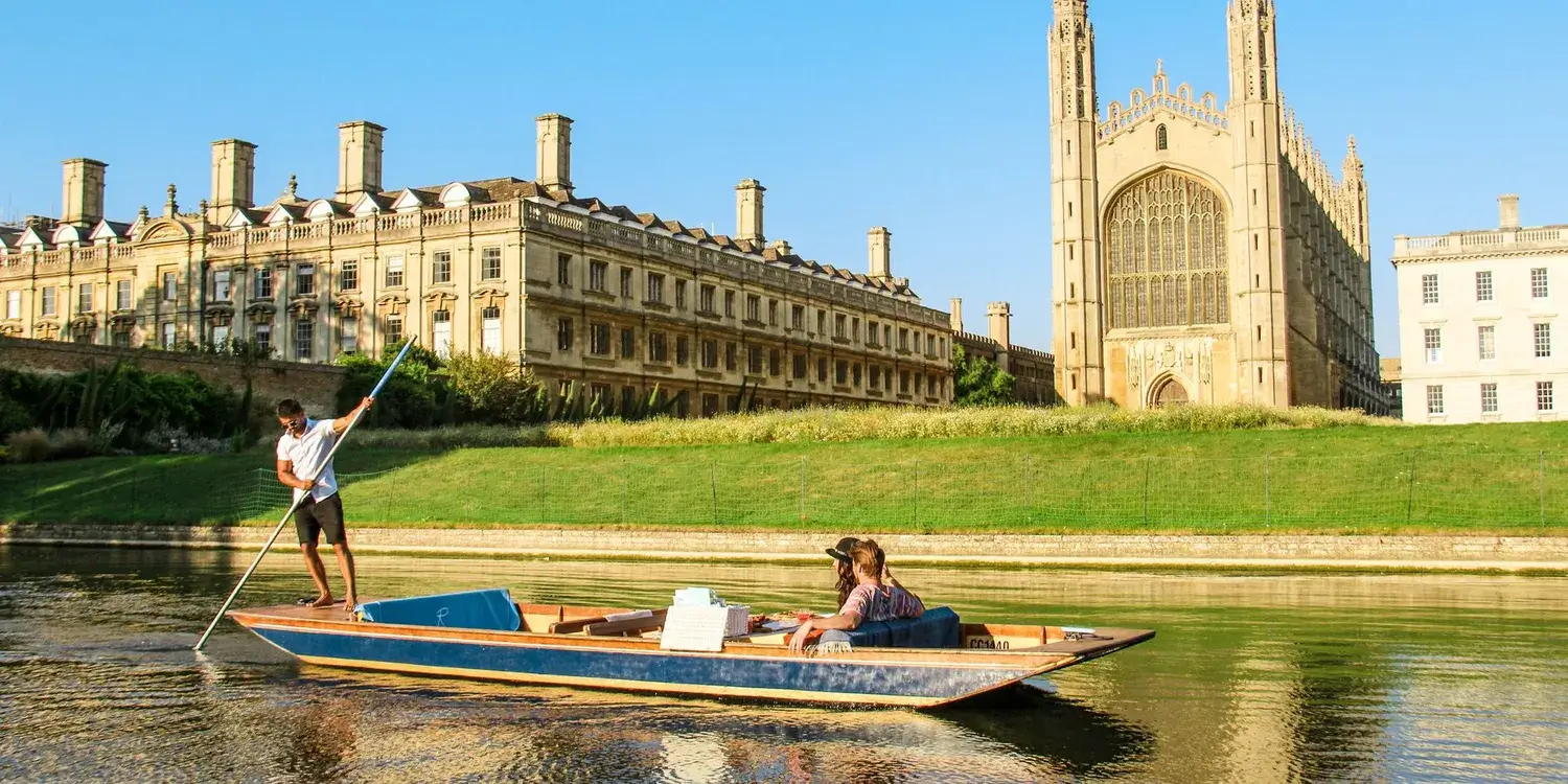 A punting boat in front of the Kings College Chapel, an impressive stone building, on a bright Summer evening.