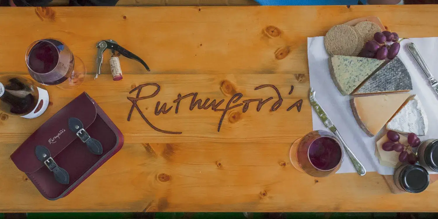 A wooden board, carved with the Rutherfords logo, holding a display of cheese, grapes and wine.