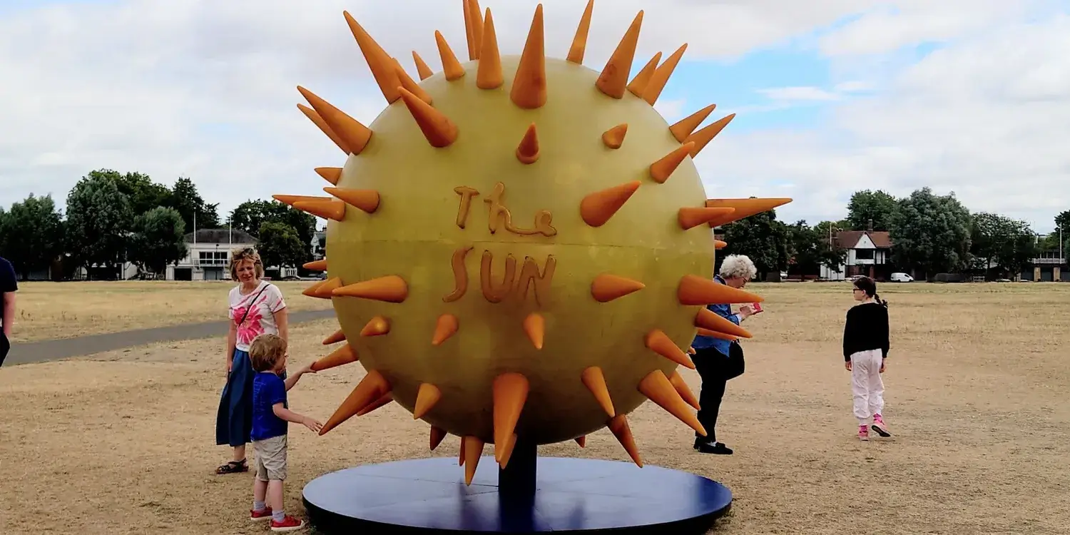 A yellow and orange sculpture of the Sun in a park in Cambridge.