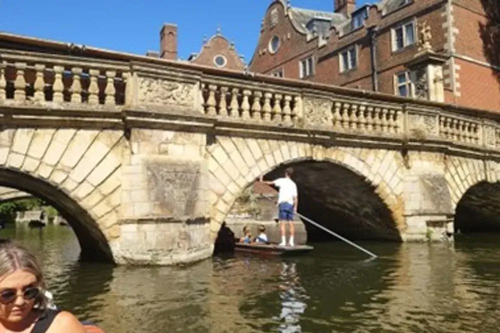 A punting boat passing under a low, arched bridge. The punting guide has to duck to pass under the bridge, hence its nickname, Concussion Bridge.