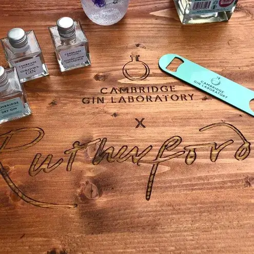 A wooden board, carved with the Rutherfords logo, holding a number of Cambridge Gin Laboratory bottles.