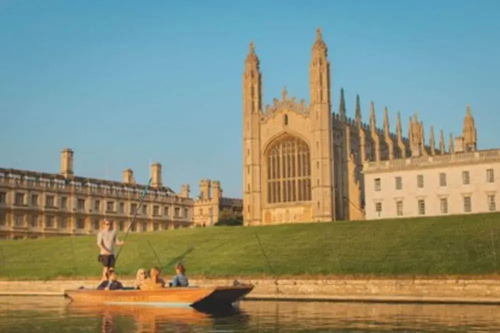 A punting boat in front of the King's College Chapel, an impressive stone building, on a bright Summer's evening.