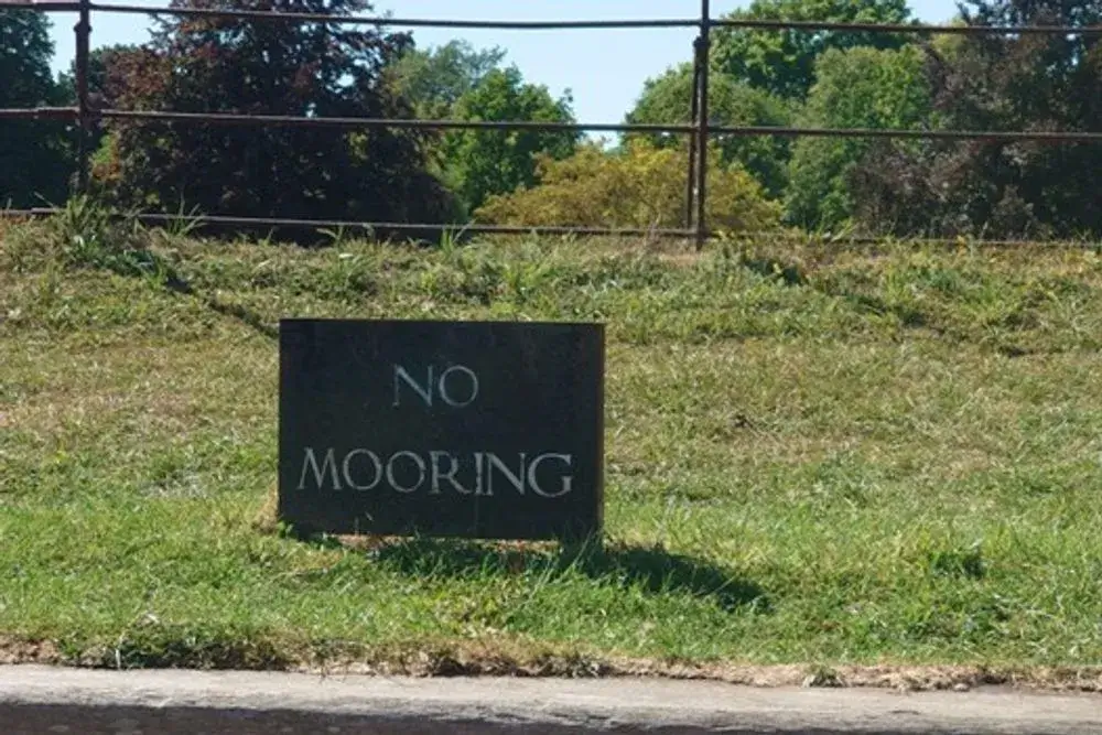 A wooden sign at the side of the river that reads 'No Mooring'.
