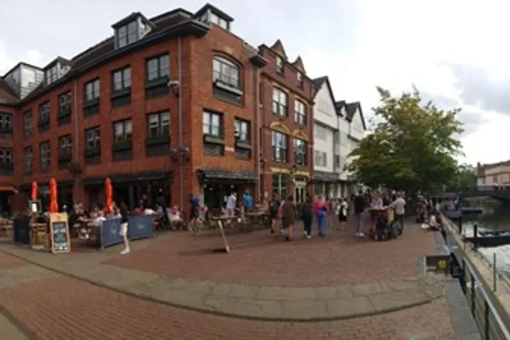 A bustling street alongside the river, where punting boats are moored.