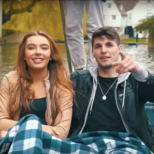 A young couple sitting in a punting boat, smiling and pointing.