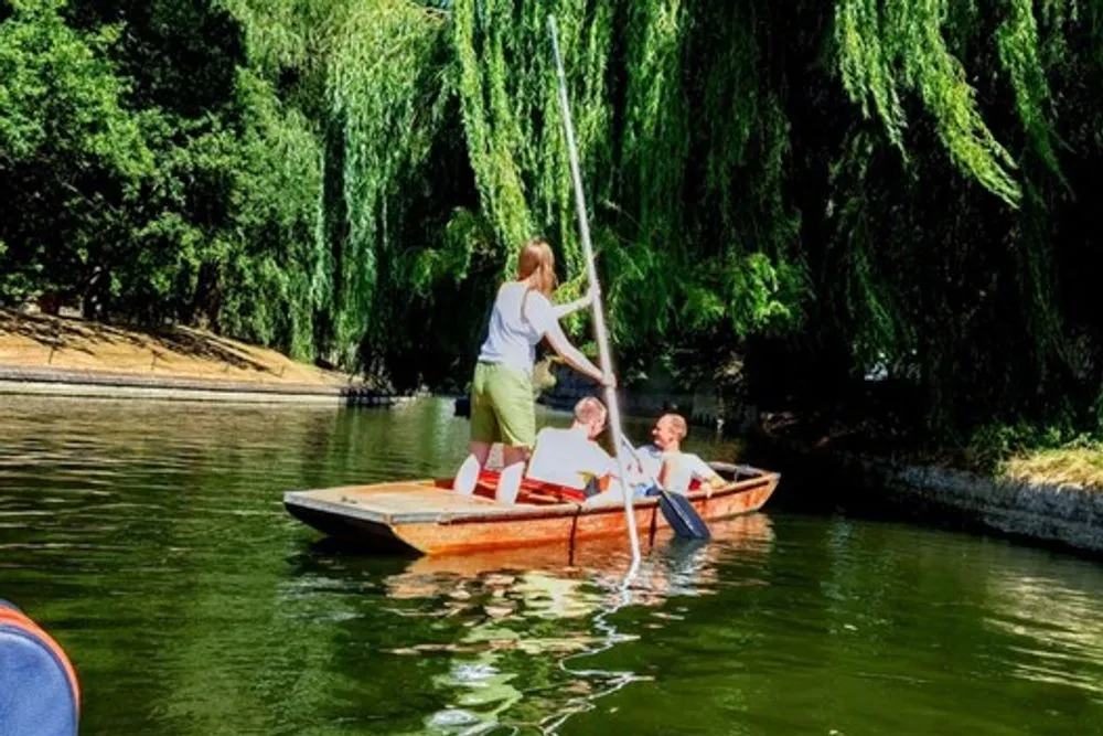 Two men sitting in a punting boat, being navigated by their punting guide beneath overhanging willow branches.