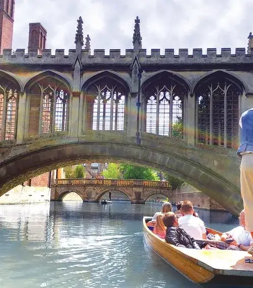 A party of people in a punting boat beneath the Bridge of Sighs, an ornately carved, arched stone bridge.