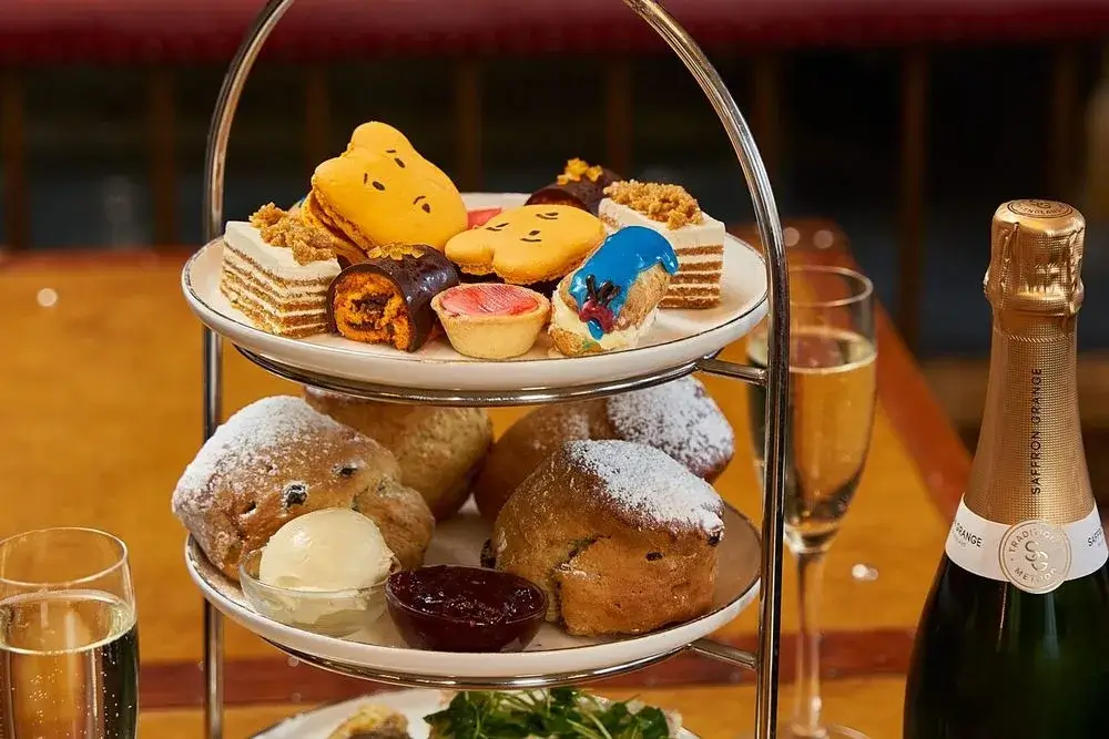 A selection of sweet cakes and scones on tiered plates, next to glasses of champagne.