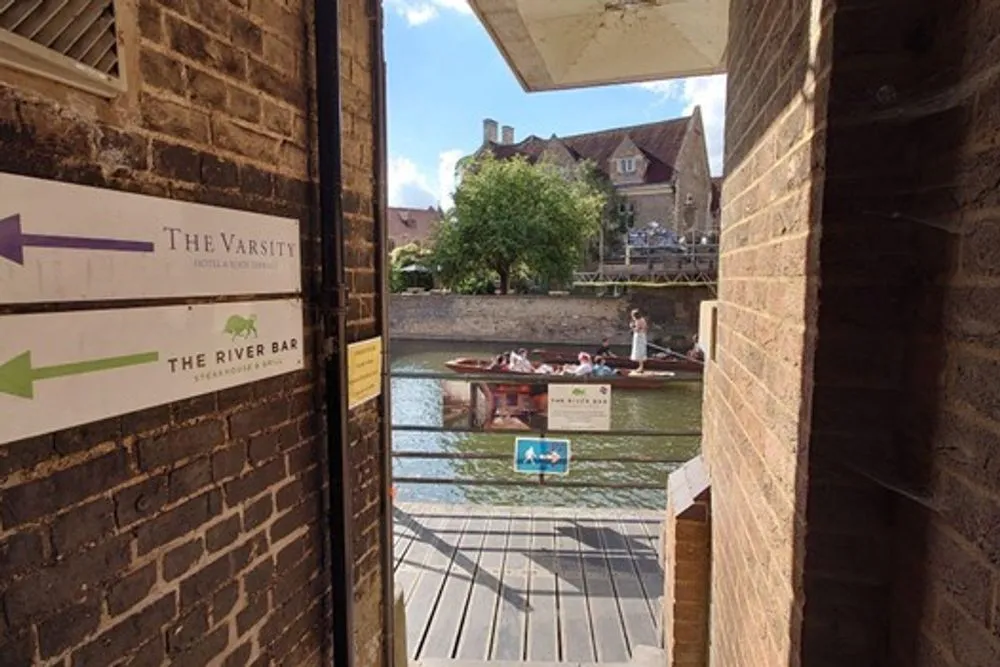 A view from a narrow alleyway leading out to the river. There are signs on the alley's wall pointing in the direction of The Varsity and The River Bar.