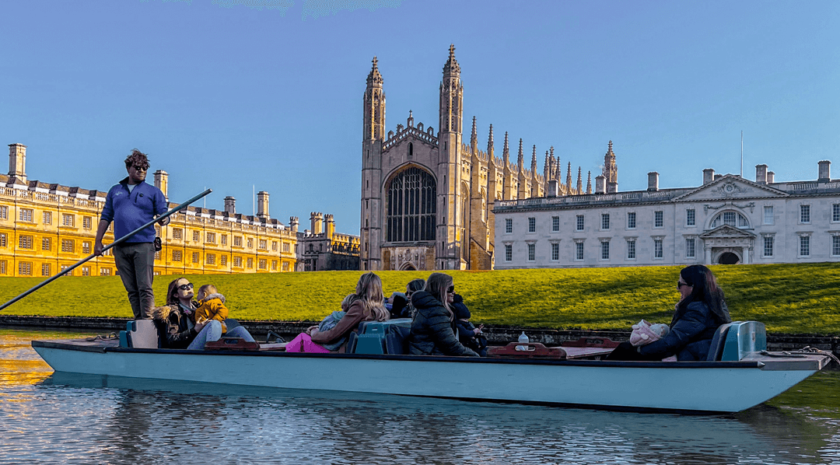 An upgraded traditional punt glides past King's College Chapel on the Cambridge College Backs. Blue skies and serene views.