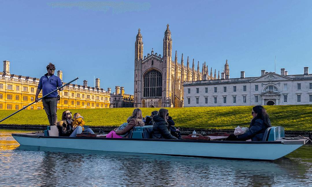 An upgraded traditional punt glides past King's College Chapel on the Cambridge College Backs. Blue skies and serene views.