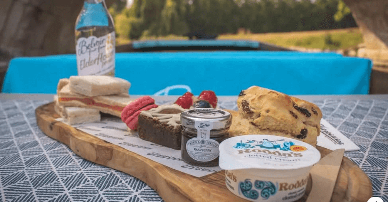 A picture of a picnic, which includes a drink and a scone, on a wooden board.