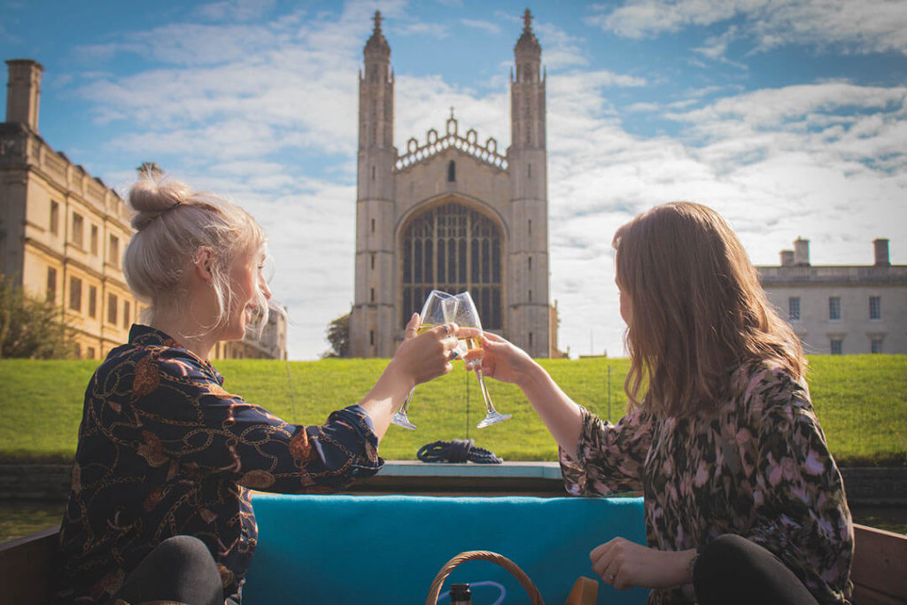 Two young women toasting champagne glasses with King's College Chapel, an impressive stone building, in the background.