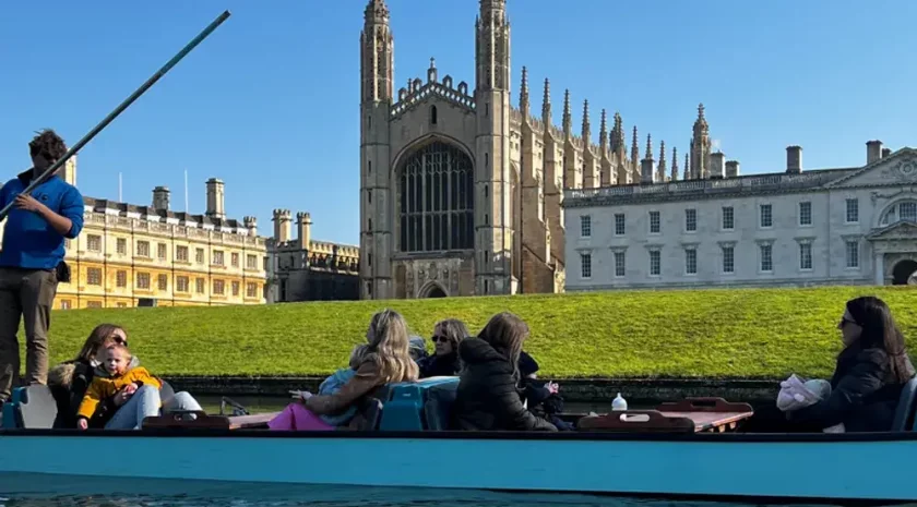 A family with children in a punting boat with Kings College Chapel, an impressive stone building, in the background.