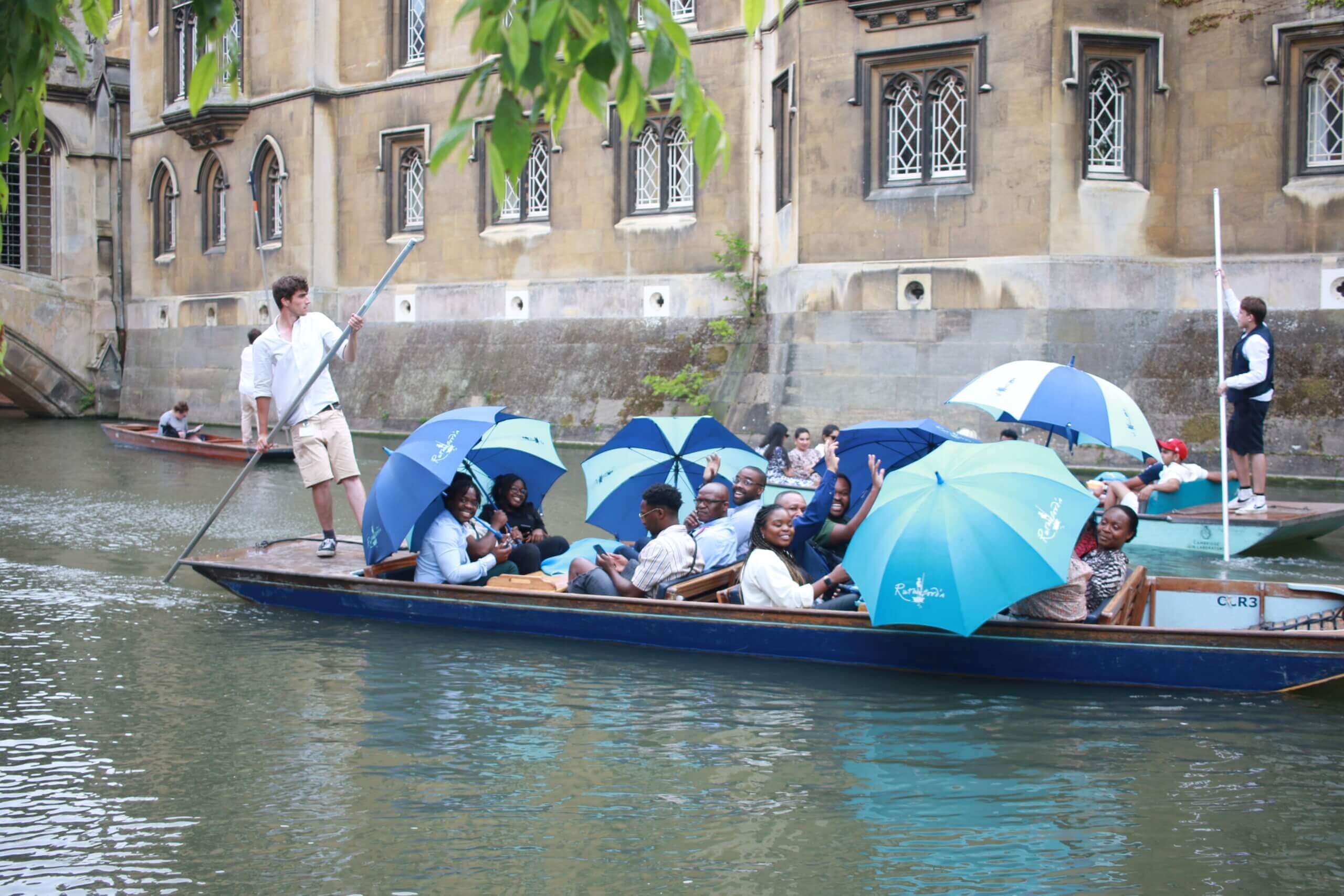 A group of people punting along the River Cam with Umbrellas out